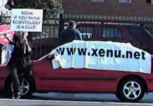 Tory Christman holding Honk if you think Scientology is a cult sign next to xenu.net banner